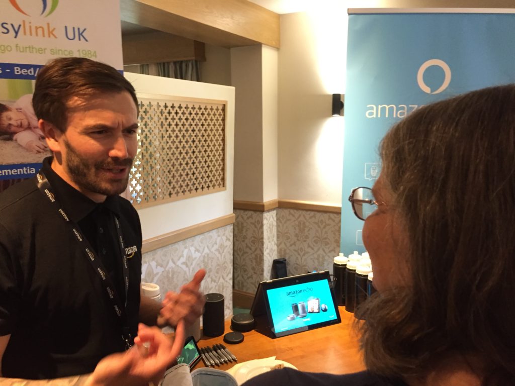 Man standing next to a table explaining to a woman about Amazon's Alexa