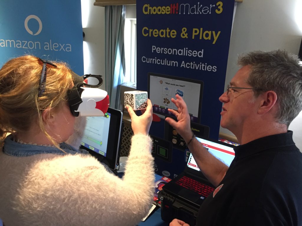 Lady wearing a virtual reality head set holding a cube with QR code in her hand. Man standing next to her explaining