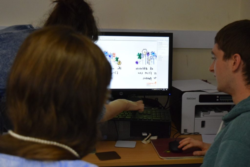 Three students sitting in front of a computer working on a design