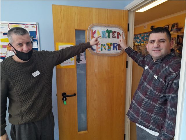 Kadr and his tutor standing in a doorway pointing to a colourful sign that says "Karten Centre"
