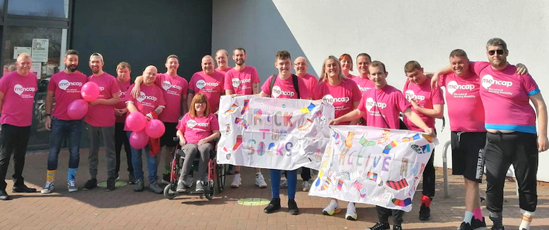 A group photo of 19 people, all wearing pink t-shirts and participating in the Rock your socks Campaign to celebrate world down syndrome day.