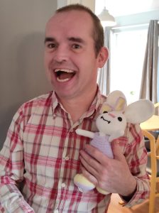 Ben standing in a doorway, holding a stuffed toy bunny and smiling 