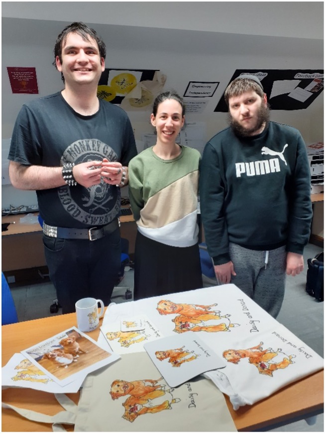 Faigie Josephs and two other students at Langdon College standing behind a table. On the table are various printed products that they have produced featuring two dogs