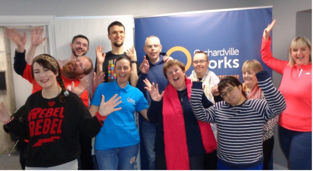 Group of staff and participants dressed in colourful outfits, standing, raising their hands in the air in celebrated Autism Awareness week.