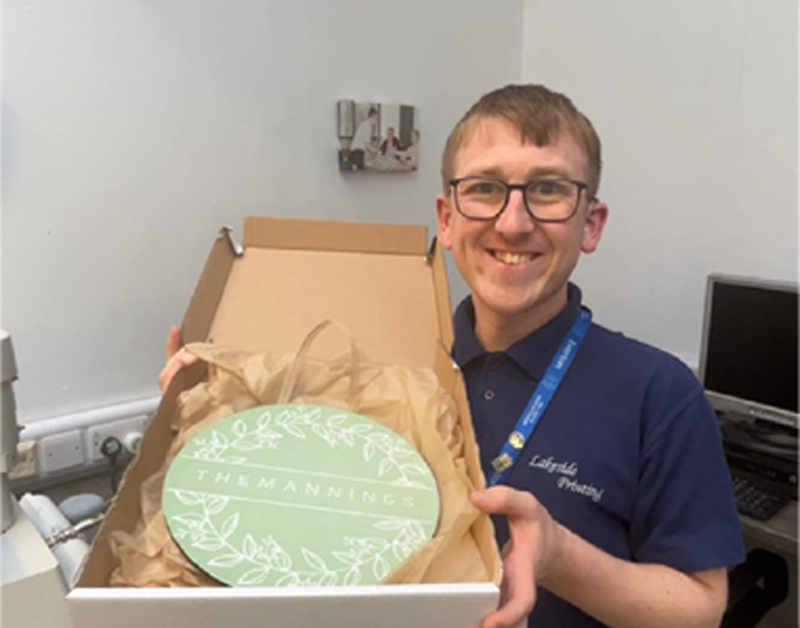 Trainee holding a completed item in a box, he has a broad smile on his face, and is beaming with pride  .
