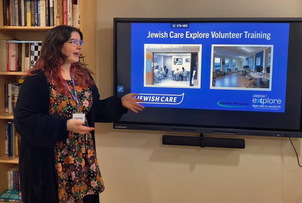 Lady standing in front of a large interactive screen talking about the Jewish Care volunteer Training 