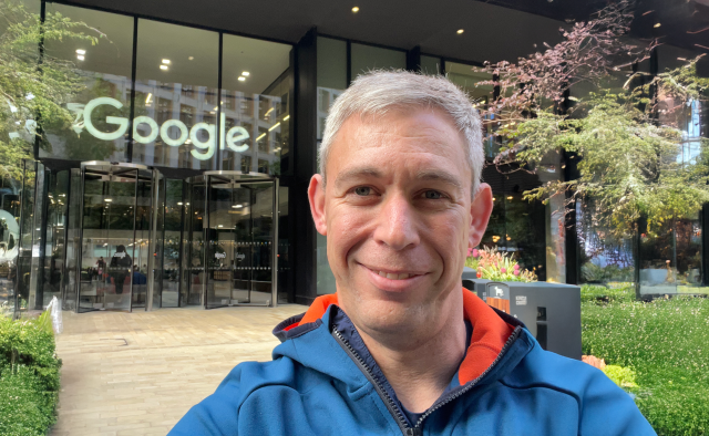 Martin Pistorius smiling outside the Google office in London, with the large Google logo visible on the glass building behind him.